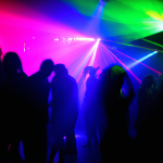 trans dance club with people dancing in silhouette with rainbow-colored lighting